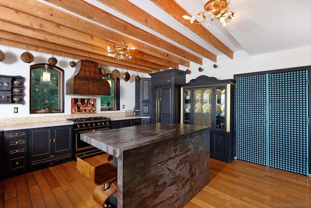 kitchen with beam ceiling, ventilation hood, light hardwood / wood-style floors, a breakfast bar area, and high end range