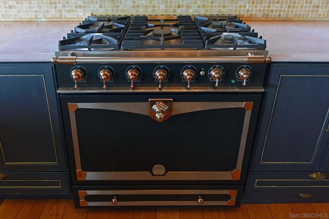 room details featuring high end range, decorative backsplash, hardwood / wood-style flooring, and blue cabinetry