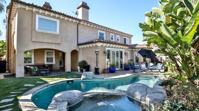 rear view of house with a chimney, stucco siding, a pool with connected hot tub, a patio area, and a tiled roof