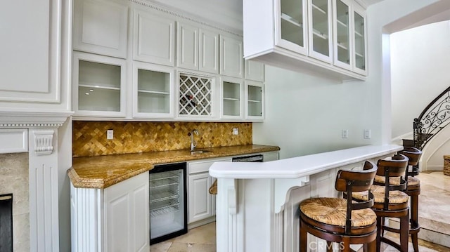 bar featuring light stone countertops, backsplash, beverage cooler, sink, and white cabinetry