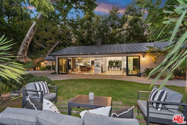 back house at dusk with outdoor lounge area, a patio area, and a yard