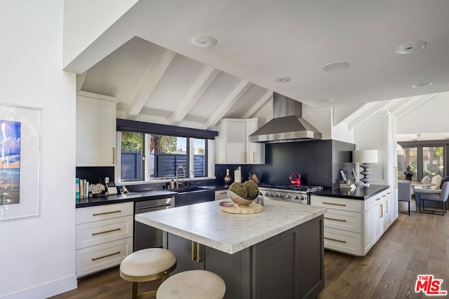 kitchen with wall chimney exhaust hood, a kitchen island, vaulted ceiling with beams, and a wealth of natural light