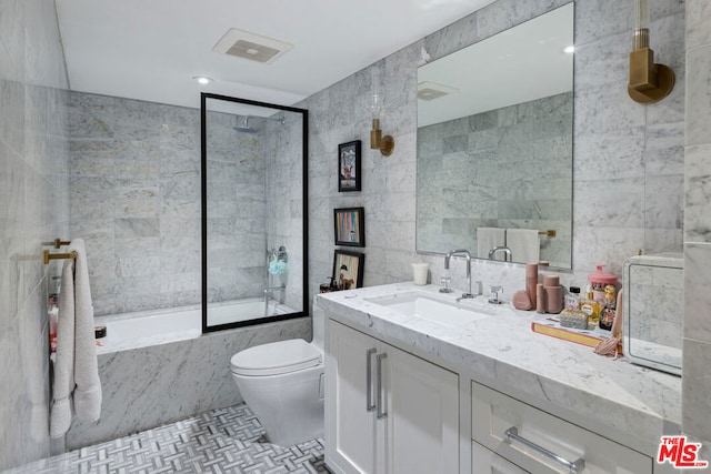 full bathroom with vanity, tiled shower / bath, toilet, and tile walls