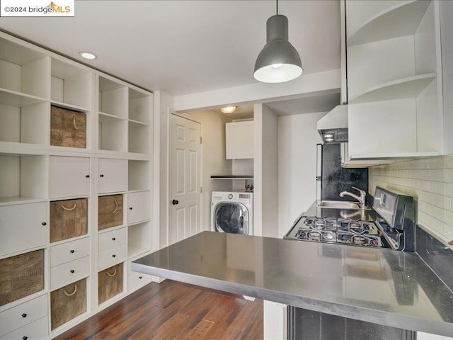 kitchen featuring wall chimney range hood, washer / clothes dryer, decorative light fixtures, white cabinetry, and dark hardwood / wood-style flooring