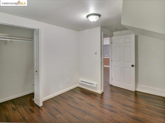 unfurnished bedroom featuring dark wood-type flooring, a closet, and a baseboard heating unit