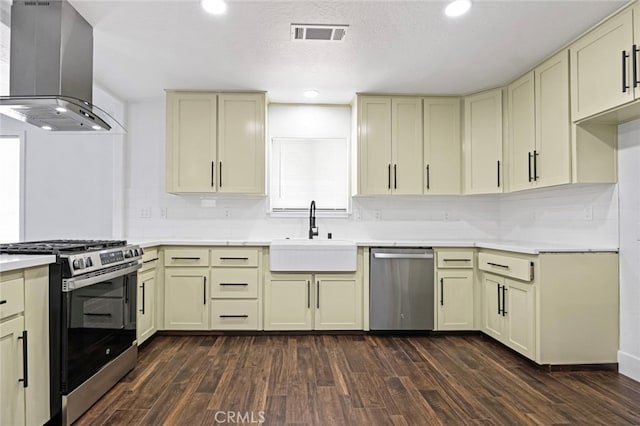 kitchen with appliances with stainless steel finishes, sink, cream cabinets, dark hardwood / wood-style flooring, and wall chimney exhaust hood