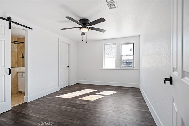 unfurnished bedroom featuring ensuite bathroom, dark hardwood / wood-style flooring, a barn door, and ceiling fan