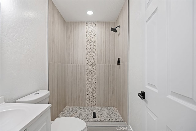 bathroom with toilet, vanity, and a tile shower