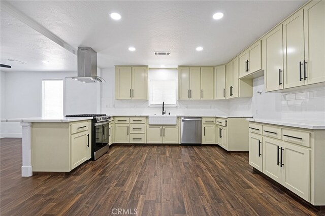 kitchen with wall chimney exhaust hood, cream cabinets, stainless steel appliances, and dark hardwood / wood-style flooring