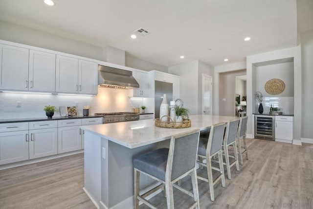 kitchen with a center island, wall chimney range hood, wine cooler, stainless steel range oven, and light wood-type flooring