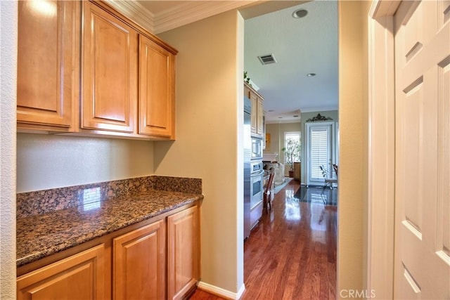 kitchen featuring dark stone countertops, dark hardwood / wood-style flooring, stainless steel appliances, and ornamental molding