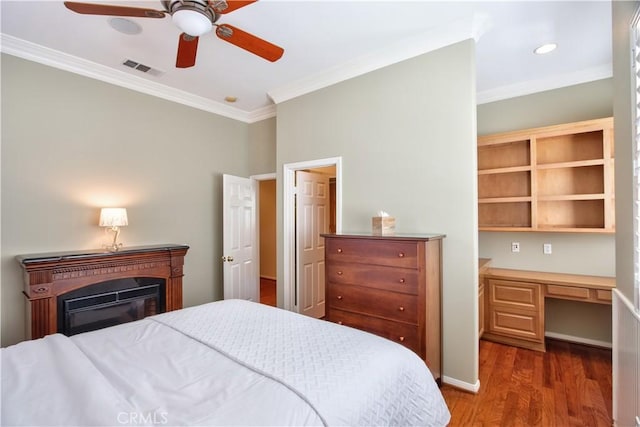 bedroom with ceiling fan, dark hardwood / wood-style flooring, built in desk, and crown molding