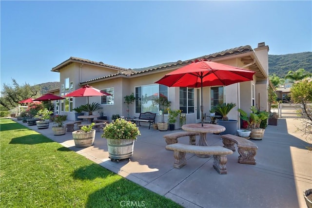 rear view of house featuring a mountain view, a patio, and a lawn