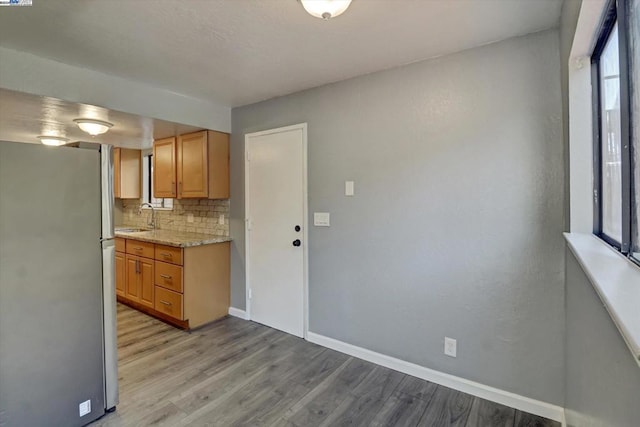 kitchen featuring tasteful backsplash, light wood-type flooring, stainless steel refrigerator, sink, and light stone counters