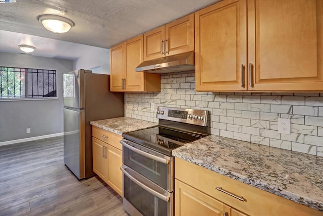 kitchen with light brown cabinets, decorative backsplash, hardwood / wood-style flooring, light stone countertops, and stainless steel appliances