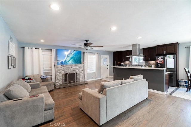 living room with ceiling fan, a stone fireplace, and hardwood / wood-style floors