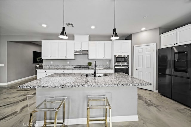 kitchen with a kitchen island with sink, black fridge, a kitchen breakfast bar, sink, and decorative light fixtures