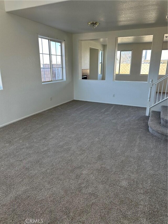 unfurnished living room featuring stairs and dark colored carpet