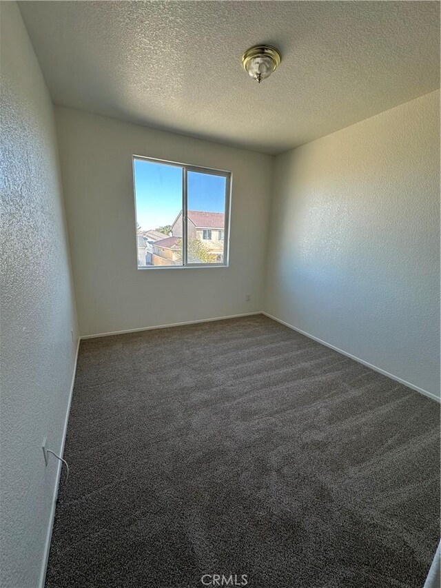 carpeted empty room featuring a textured wall, baseboards, and a textured ceiling