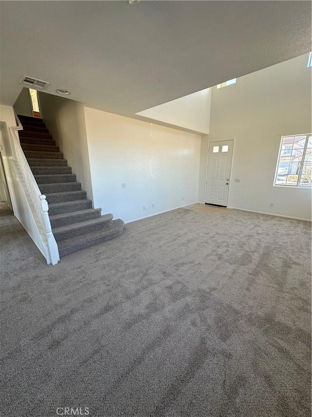 unfurnished living room featuring visible vents, carpet floors, a high ceiling, and stairs