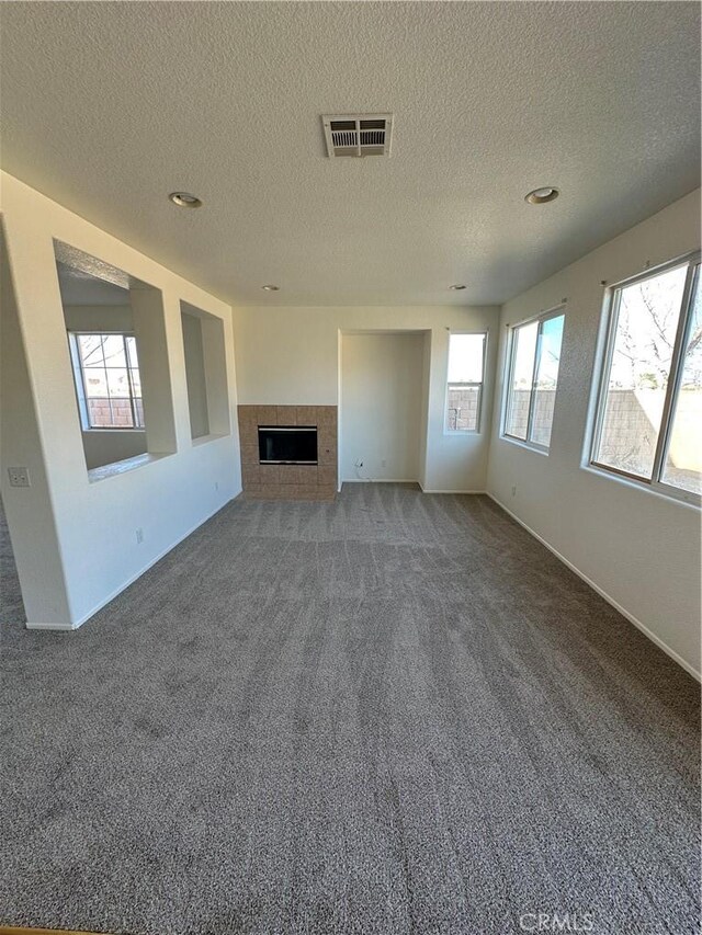 unfurnished living room with a tiled fireplace, visible vents, a healthy amount of sunlight, and carpet floors