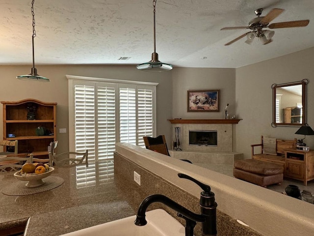 living room with a textured ceiling, ceiling fan, a fireplace, and vaulted ceiling