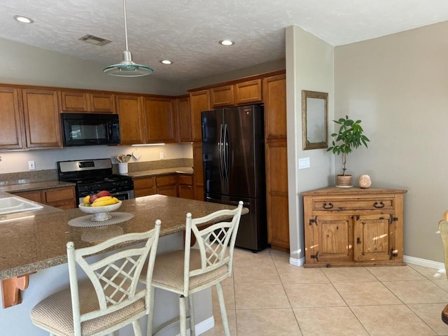 kitchen with stainless steel gas range, refrigerator, decorative light fixtures, a breakfast bar, and light tile patterned flooring