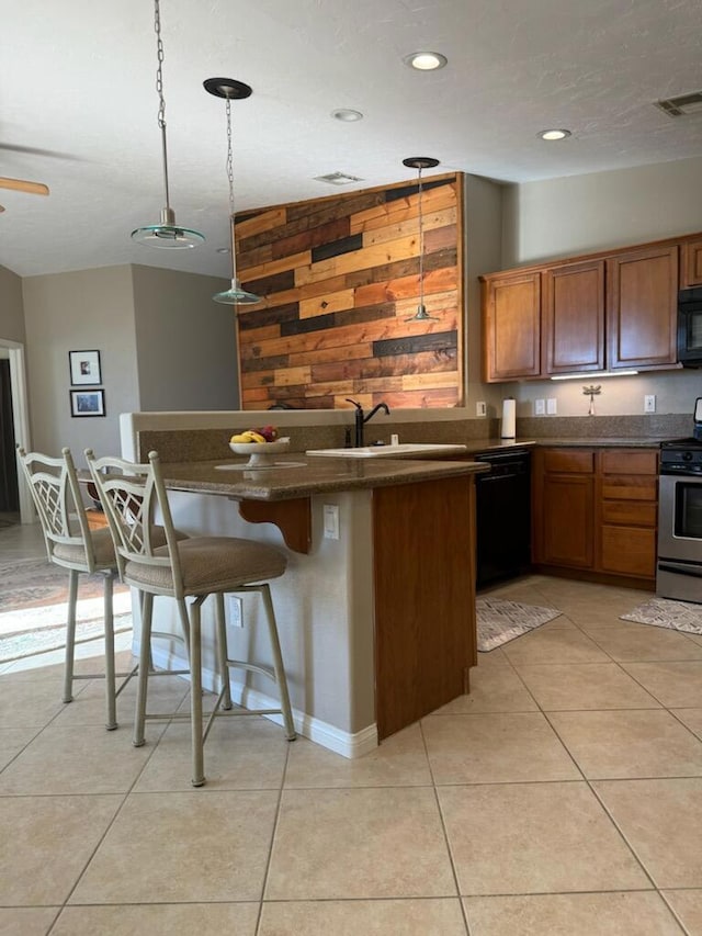 kitchen with sink, hanging light fixtures, a breakfast bar area, light tile patterned floors, and black appliances