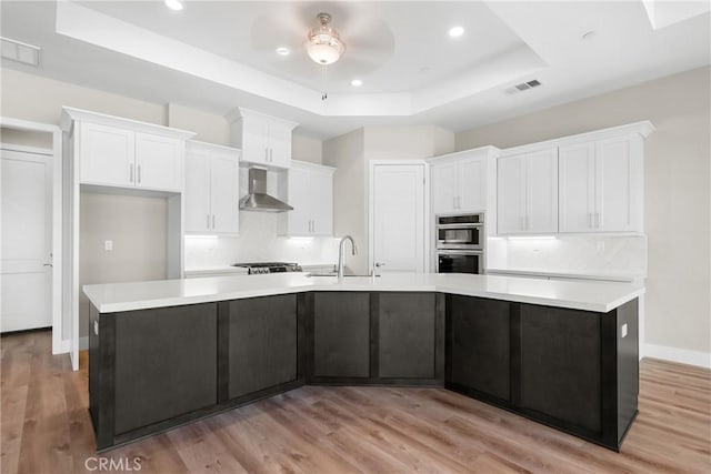 26176 Boulder View Ct, Menifee, CA 92584 - kitchen with wall chimney exhaust hood, a raised ceiling, double oven, white cabinetry, and a large island with sink