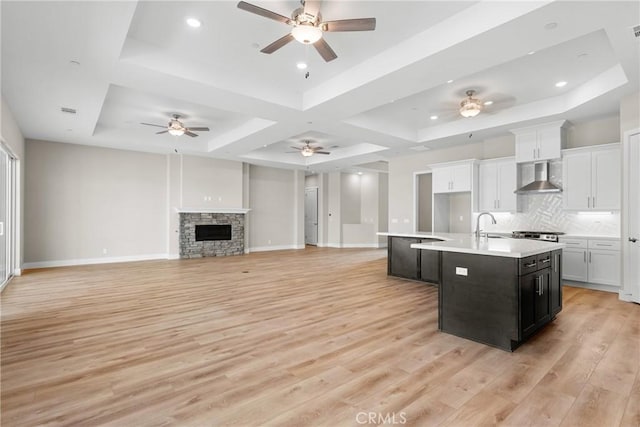 26176 Boulder View Ct, Menifee, CA 92584 - kitchen with wall chimney range hood, an island with sink, a tray ceiling, light wood-style floors, and recessed lighting