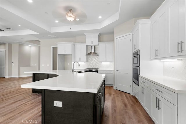 26176 Boulder View Ct, Menifee, CA 92584 - kitchen with light wood-style flooring, tasteful backsplash, a tray ceiling, a ceiling fan, and wall chimney range hood