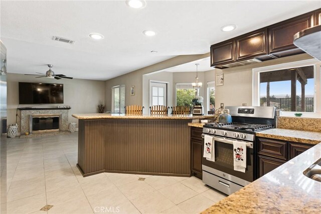 kitchen with hanging light fixtures, a wealth of natural light, dark brown cabinetry, and stainless steel gas range oven