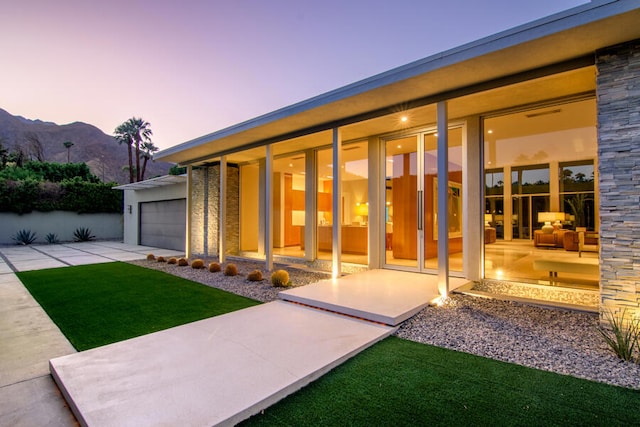 exterior entry at dusk with a mountain view, a garage, and a yard