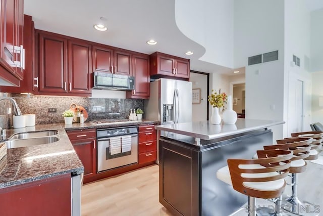 kitchen featuring appliances with stainless steel finishes, light wood-type flooring, sink, a towering ceiling, and a center island