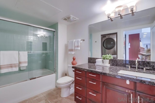 full bathroom with combined bath / shower with glass door, stacked washing maching and dryer, toilet, vanity, and tile patterned floors