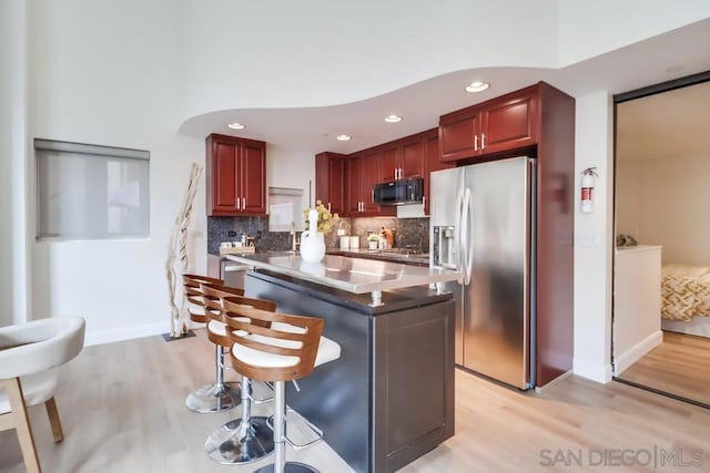 kitchen featuring light hardwood / wood-style flooring, backsplash, a breakfast bar, a center island, and stainless steel fridge with ice dispenser