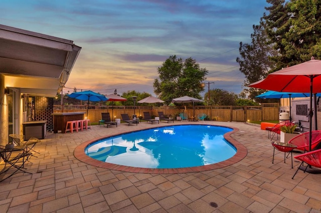 pool at dusk featuring a patio area and an outdoor bar