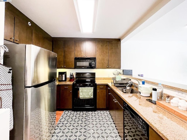 kitchen with dark brown cabinets, light stone countertops, black appliances, and sink