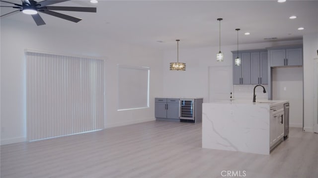 kitchen featuring light stone counters, sink, light hardwood / wood-style floors, wine cooler, and an island with sink