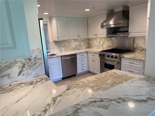 kitchen featuring appliances with stainless steel finishes, white cabinetry, light stone counters, and wall chimney range hood