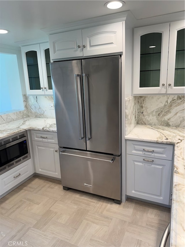 kitchen featuring white cabinetry, light stone counters, stainless steel appliances, and backsplash