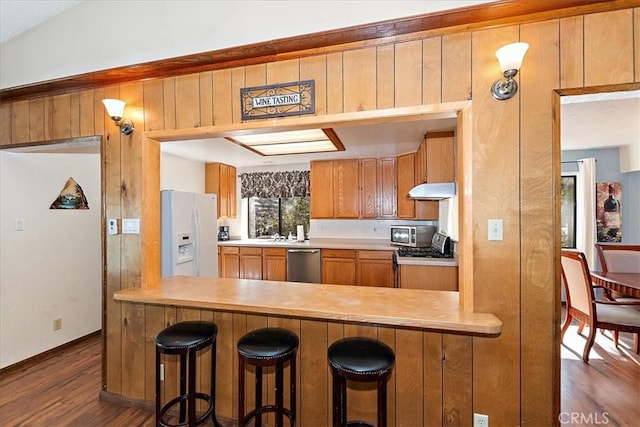 kitchen with dark hardwood / wood-style flooring, stainless steel dishwasher, white refrigerator with ice dispenser, kitchen peninsula, and a kitchen bar