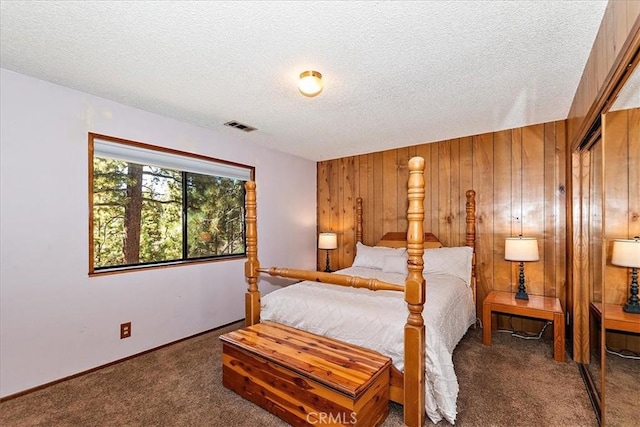 bedroom with dark colored carpet, a textured ceiling, and wooden walls