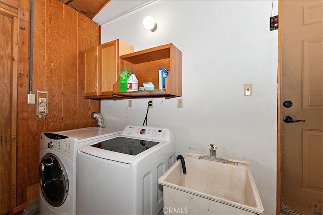 clothes washing area featuring washer and clothes dryer, cabinets, sink, and wooden walls