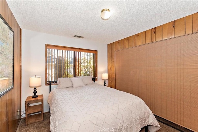 carpeted bedroom with a textured ceiling and wooden walls