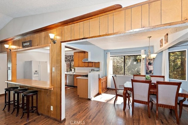 kitchen featuring white fridge with ice dispenser, dark wood-type flooring, stainless steel dishwasher, a notable chandelier, and vaulted ceiling