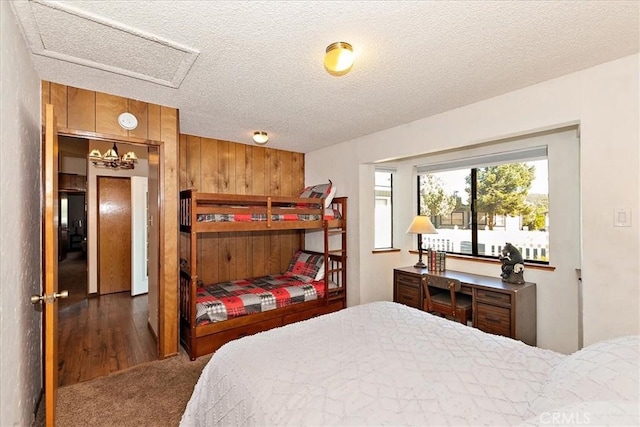 bedroom featuring wooden walls, a textured ceiling, and dark colored carpet