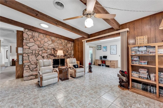 living room featuring ceiling fan, wooden walls, beam ceiling, and a textured ceiling