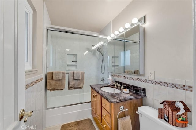 full bathroom featuring vanity, tile walls, shower / bath combination with glass door, and toilet