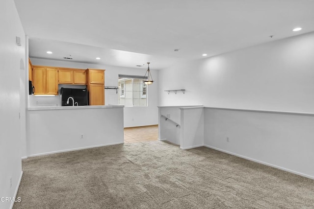 kitchen featuring light brown cabinetry, black fridge, hanging light fixtures, and light carpet